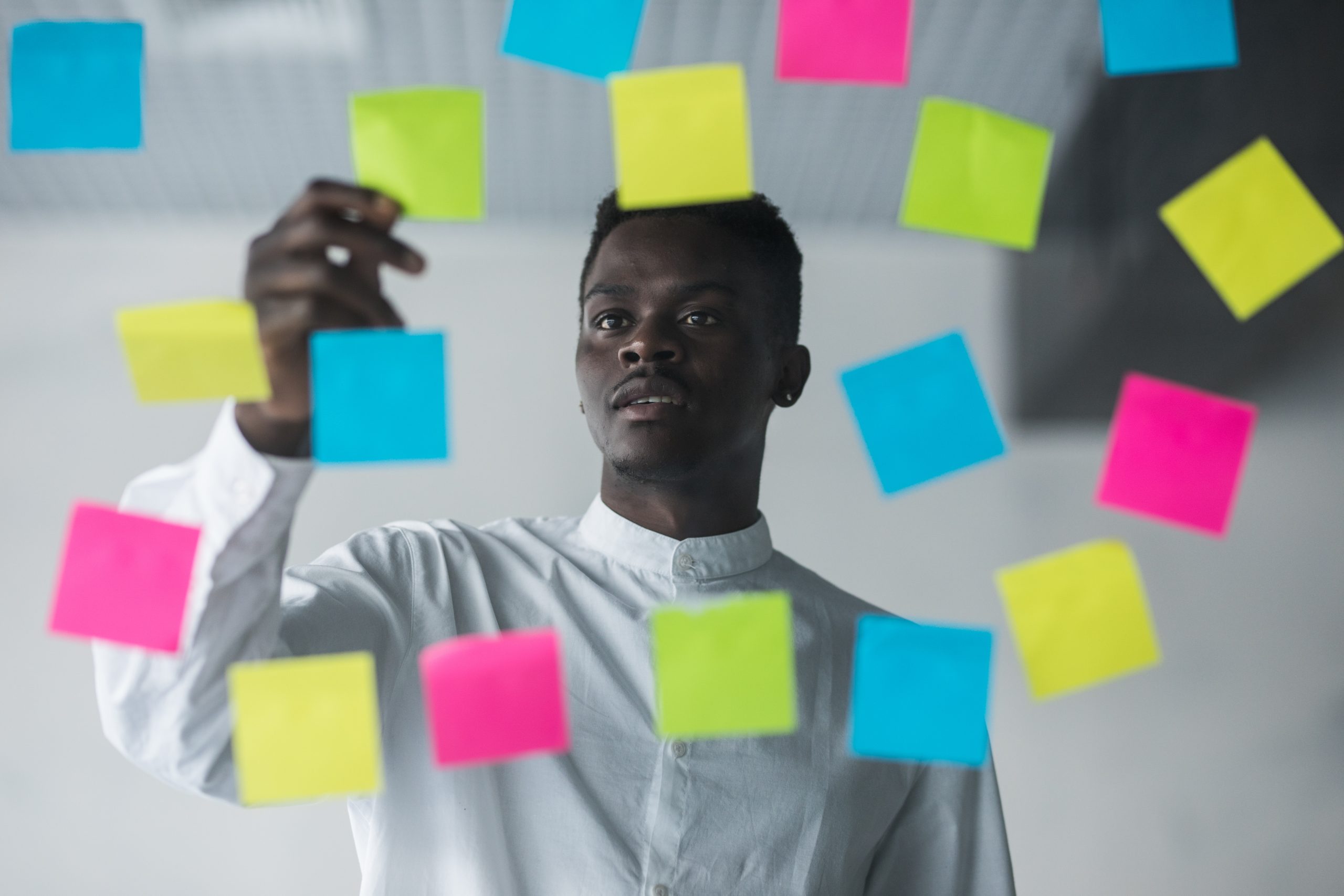 Young afro american business man standing in front of stickers g Young afro american business man standing in front of stickers glass wall and write task on sticker at his office place